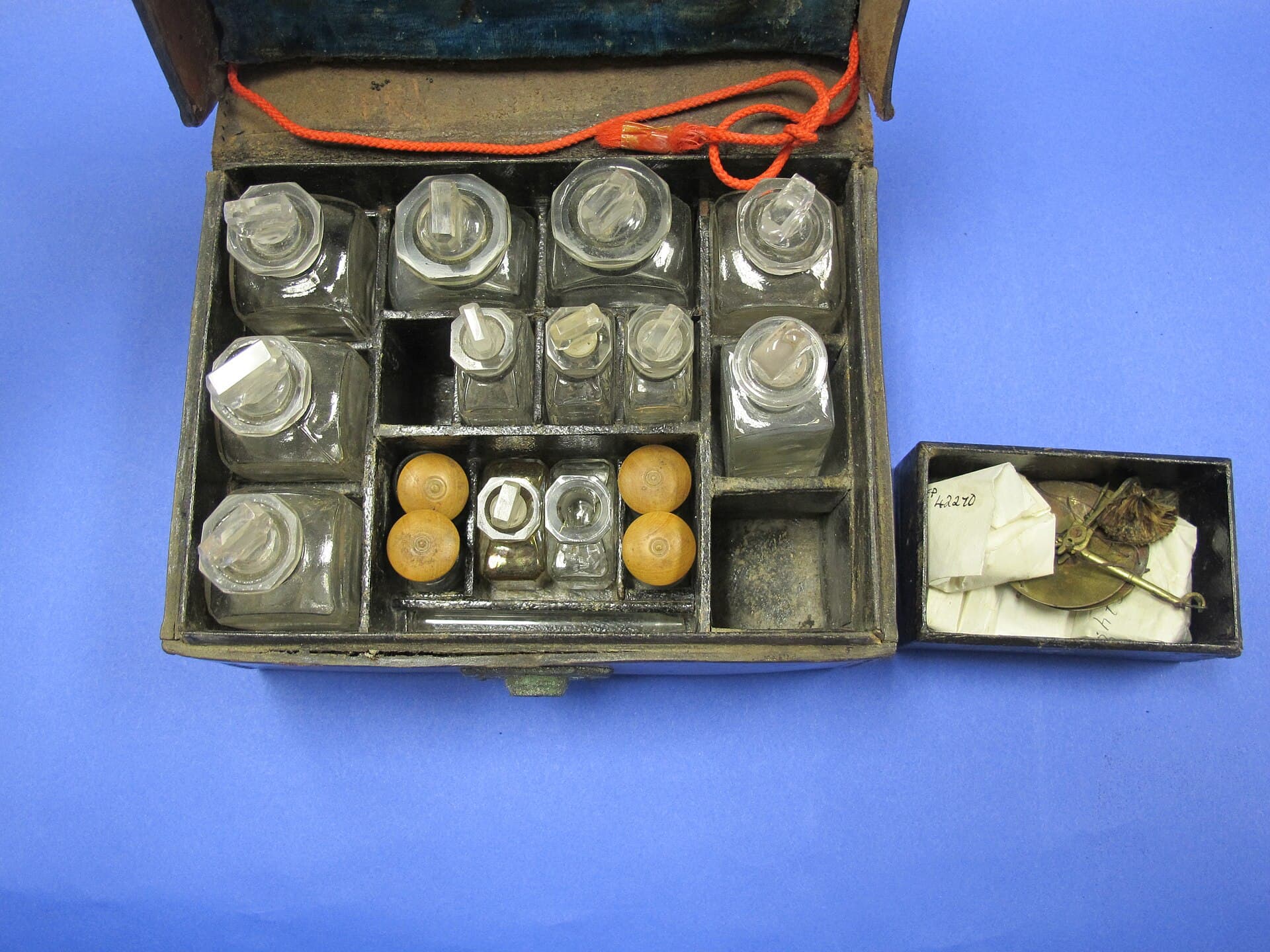 A museum assay set: a wooden case of glass reagent bottles with a small balance